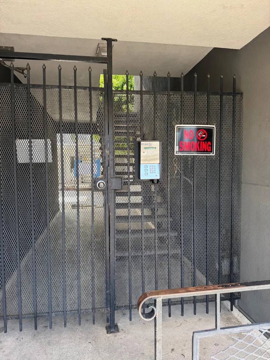 DoorKing intercom and keypad mounted on a black metal pedestrian gate with mesh panels