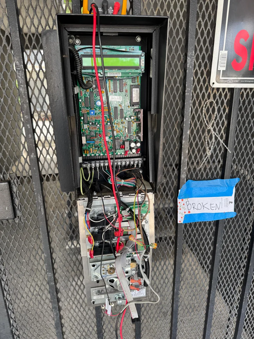 Open DoorKing intercom housing showing its control board, display and test leads at a metal gate