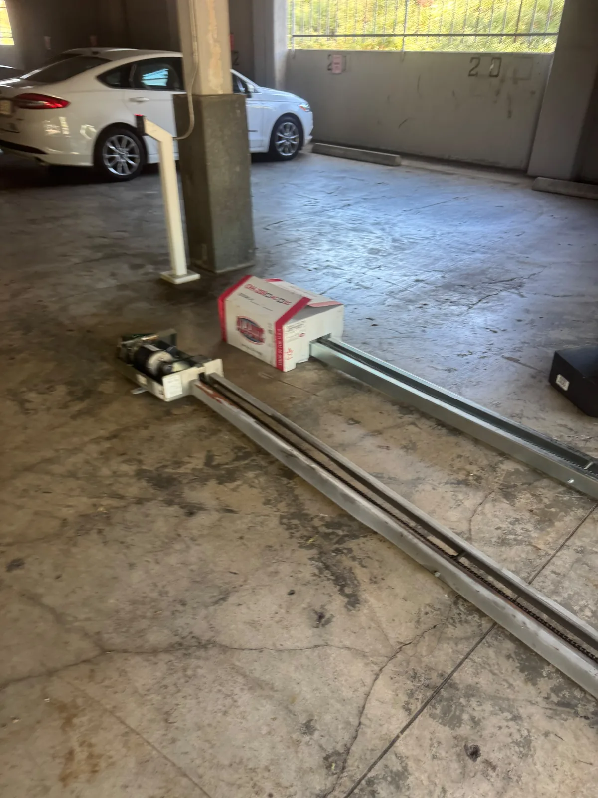 Garage opener equipment and long metal rails laid out on a concrete parking garage floor