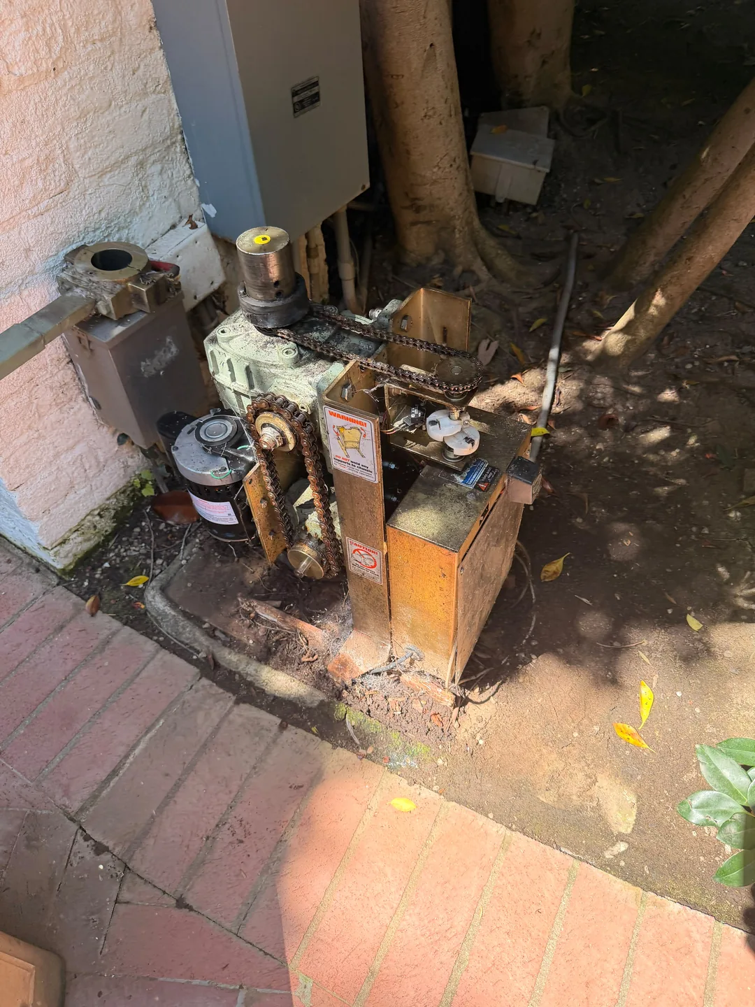 Exposed gate operator chains, sprockets and motor components beside a wall and paved path