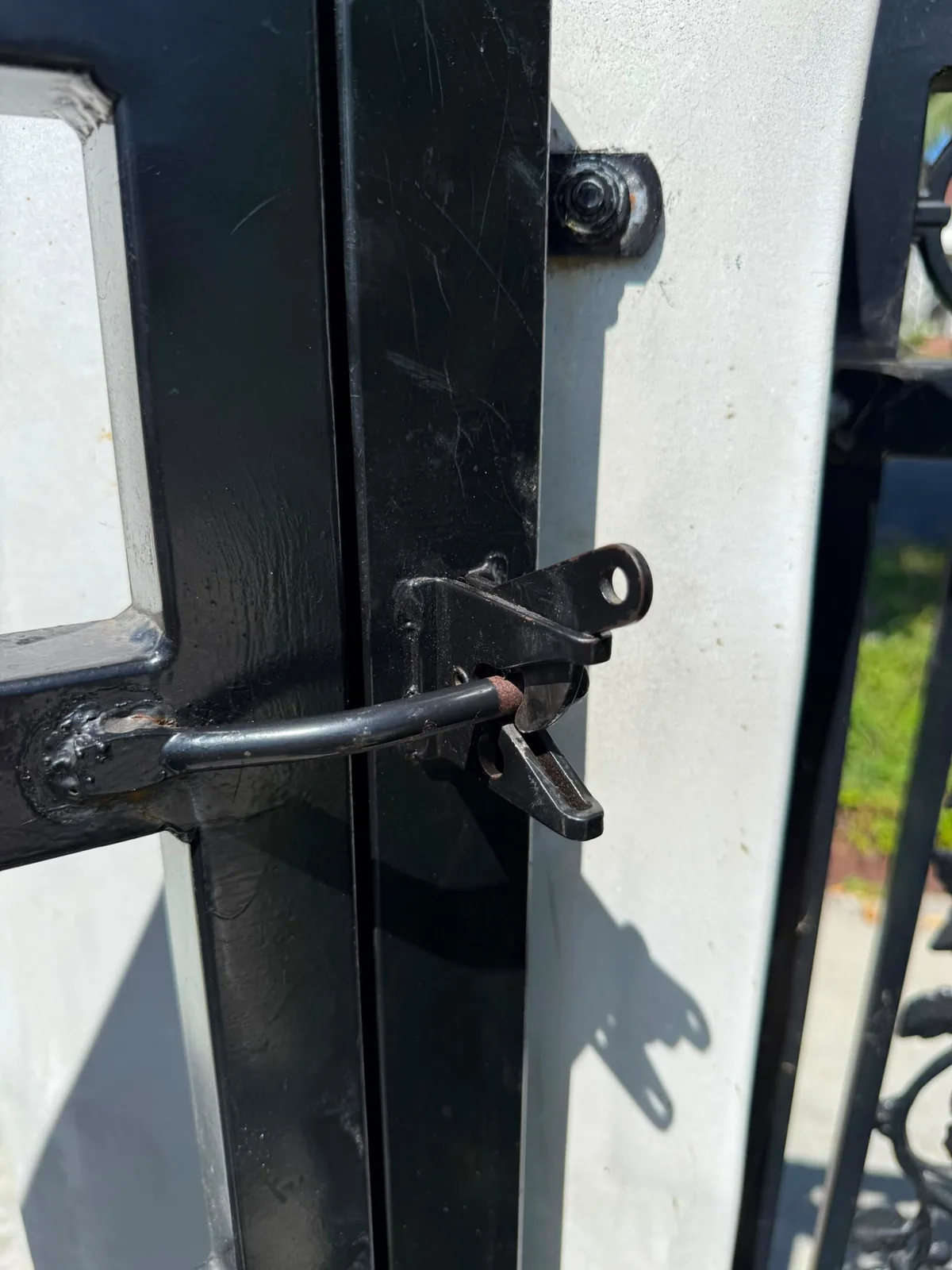 Close view of a metal gate latch and welded attachment beside a light colored gate post