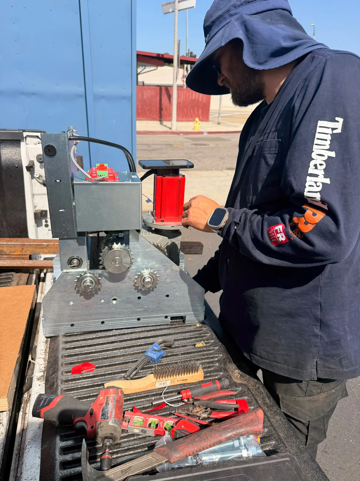 Technician working beside a red gate motor and exposed operator drive assembly on a truck bed