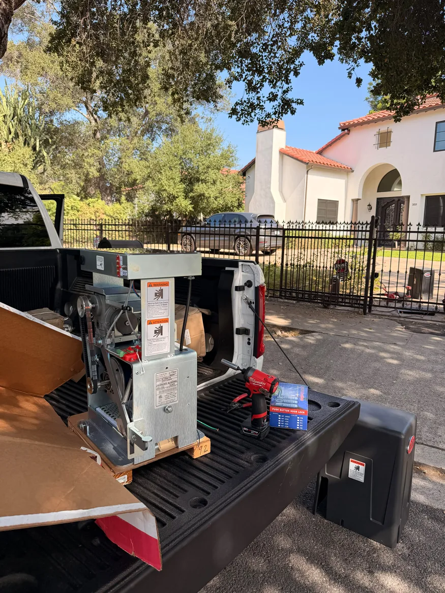 Gate operator assembly and hand tools on a pickup truck beside a residential driveway gate