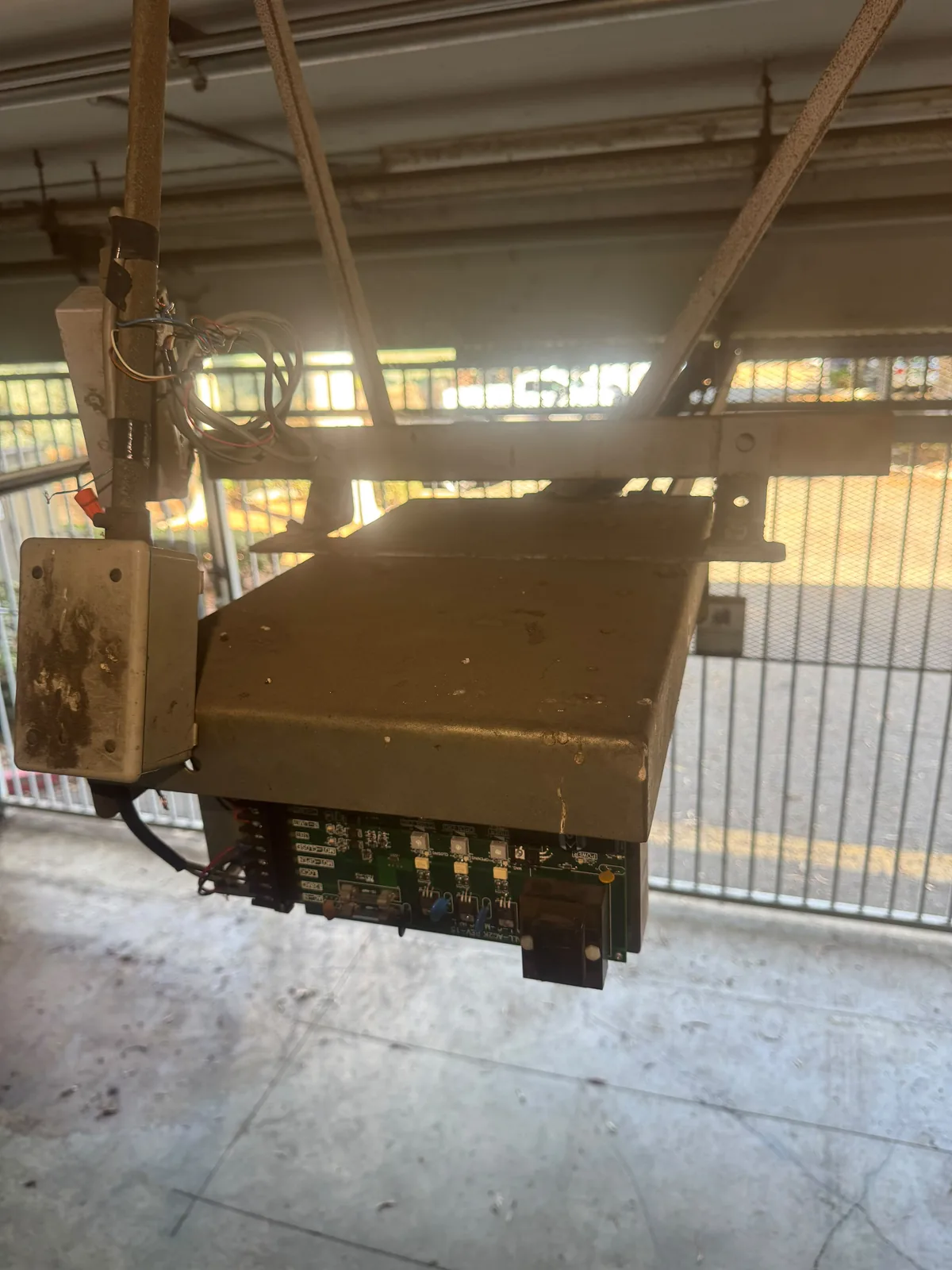 Overhead entrance operator with its control board exposed inside a shared parking garage