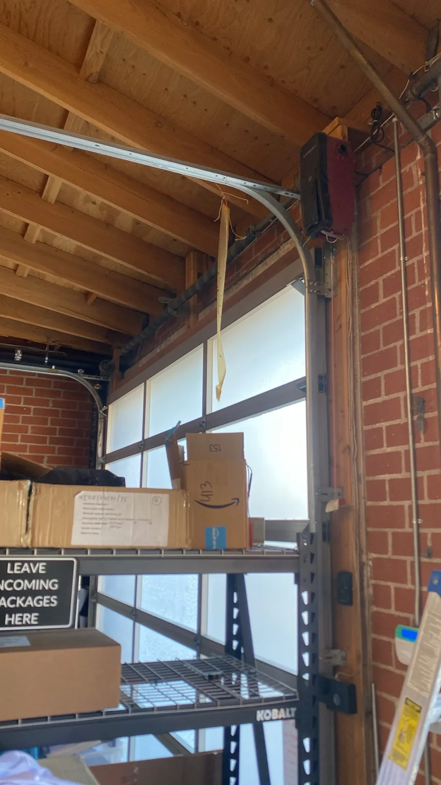 Wall mounted garage door opener beside a sectional door and curved metal track in a brick garage