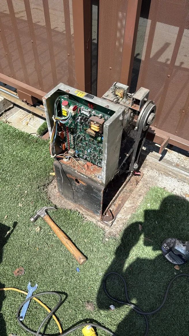 Open sliding gate operator showing its control board and drive components beside a metal gate