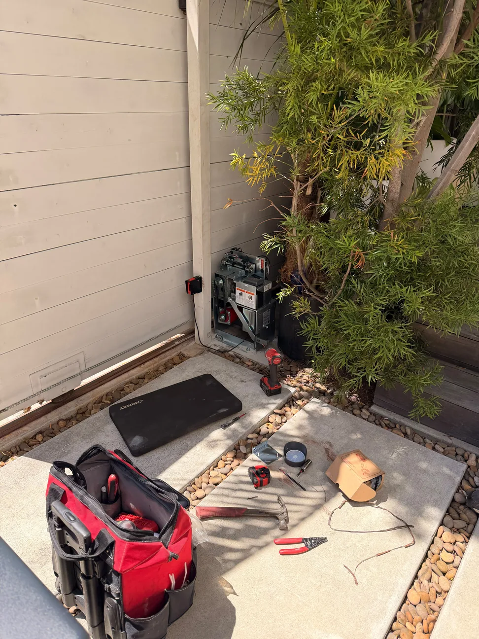 Open sliding gate operator beside a light colored driveway gate with service tools nearby